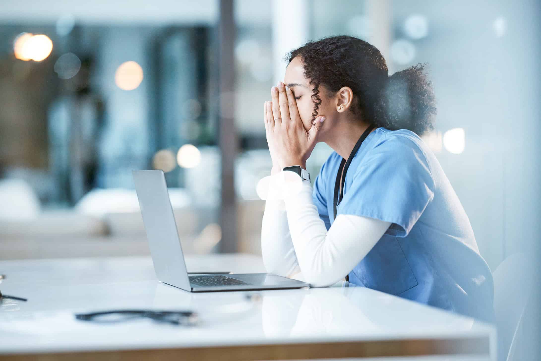 A healthcare provider sitting at a computer who is visibly frustrated with charting and documentation work.